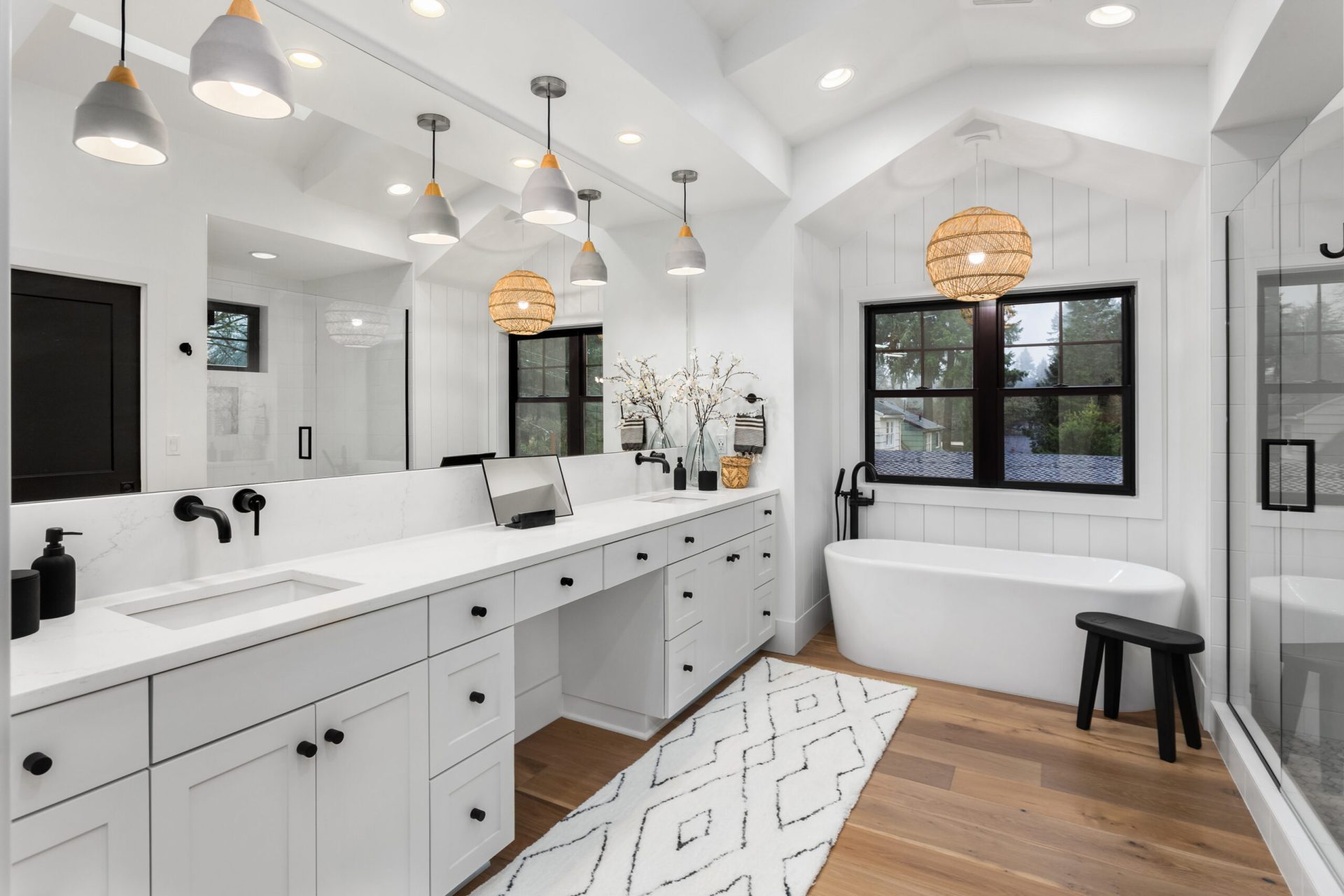 Bright white bathroom with double vanity, freestanding soaking tub, black fixtures, and wood flooring, remodeled by Dorsey Builders in Dothan, AL.