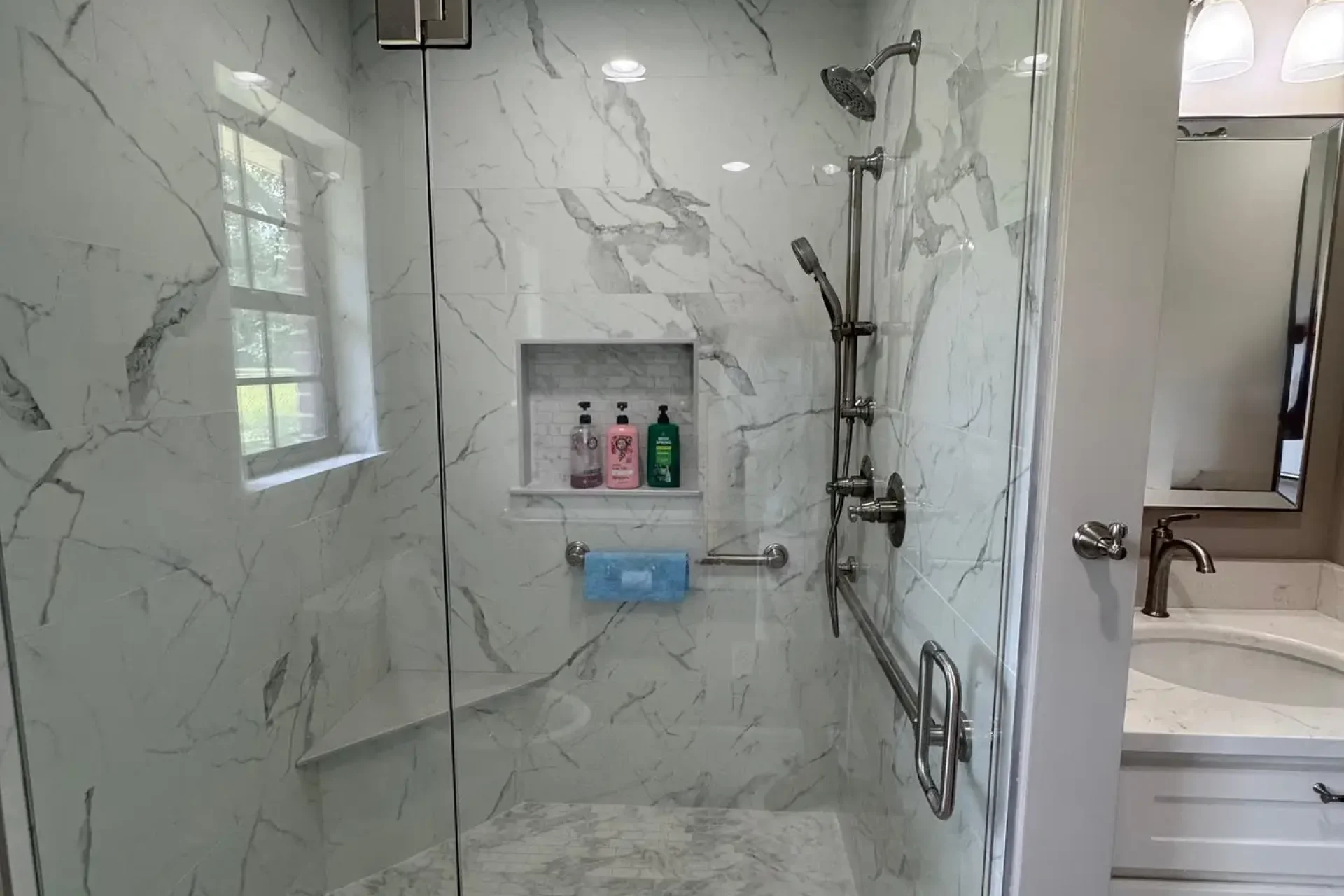 Walk-in shower with marble tile walls, frameless glass enclosure, built-in niche, and chrome fixtures, completed by Dorsey Builders in Dothan, AL.