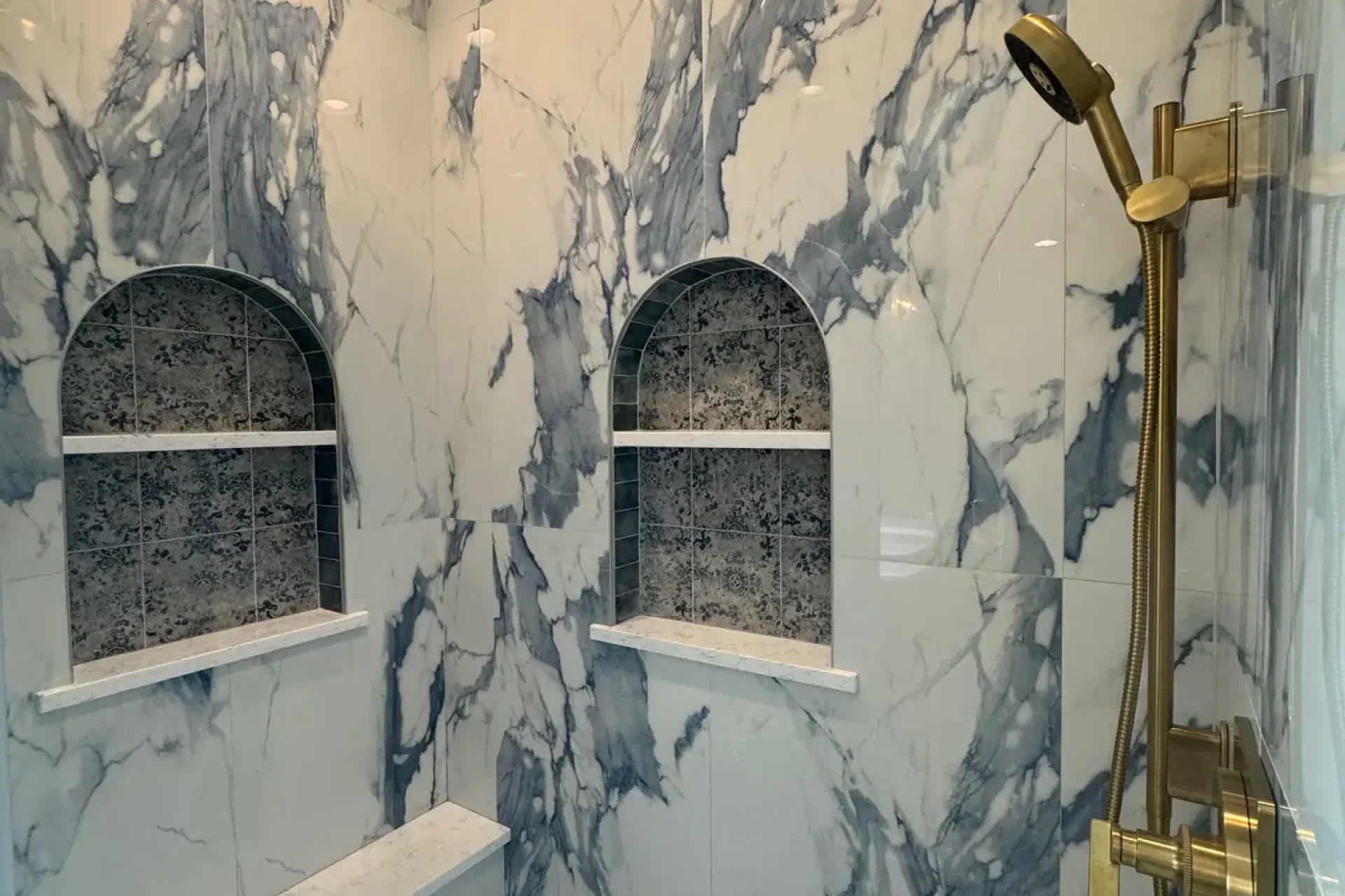 Custom shower fixtures, marble shower interior with niche shelving, and hexagon tile floor by Dorsey Builders in Dothan, Alabama.