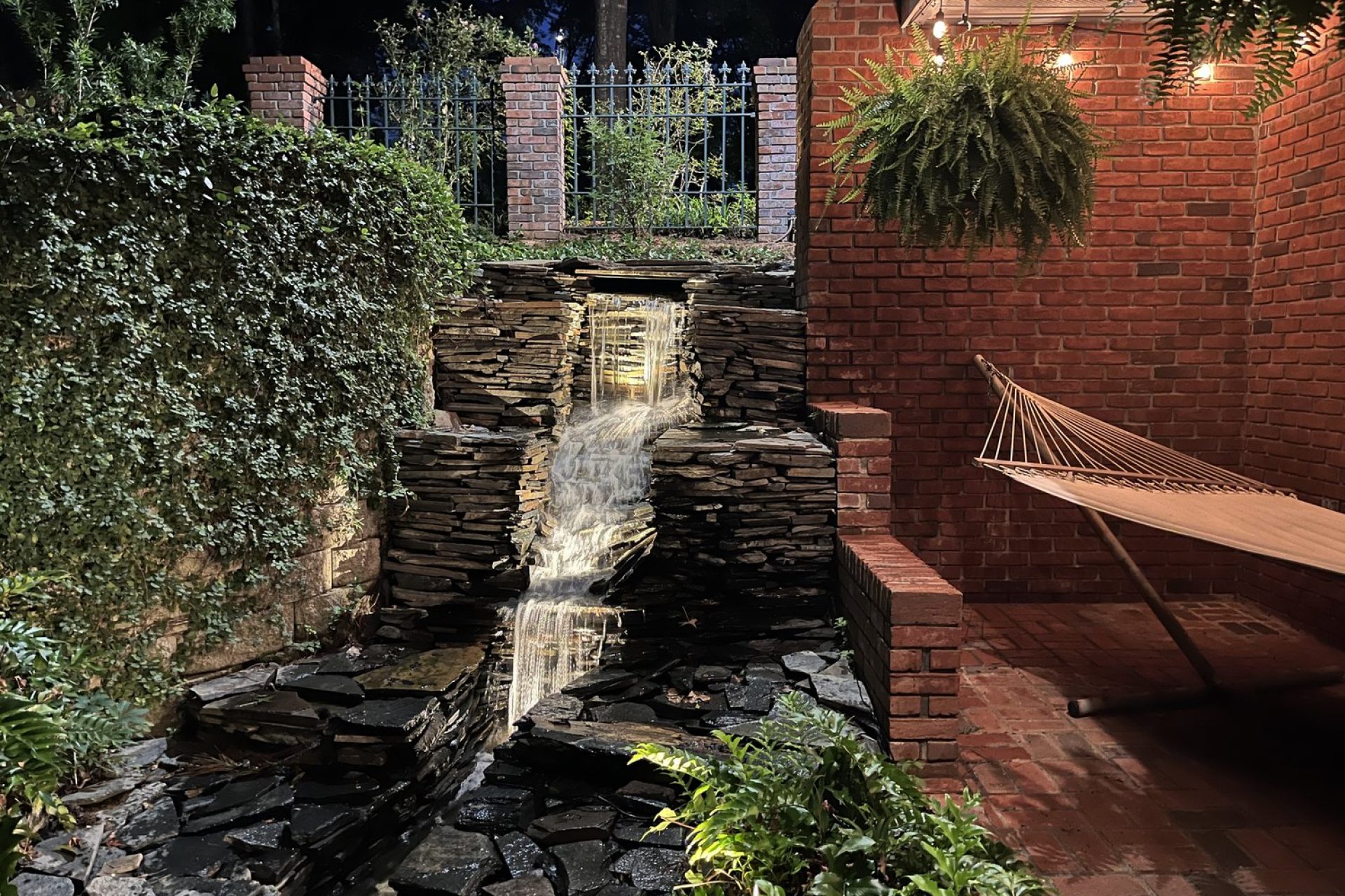 Custom outdoor waterfall feature with stacked stone, brick patio, and relaxing hammock area, designed by Dorsey Builders, outdoor living specialists in Dothan, AL.