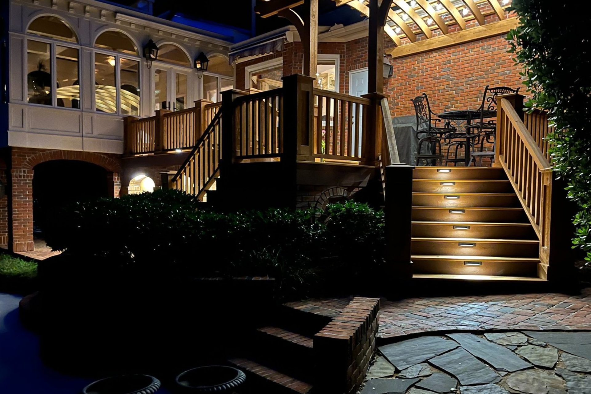 Custom-built outdoor living space in Dothan, AL, featuring illuminated wood deck stairs, pergola, and elegant brick architecture by Dorsey Builders.
