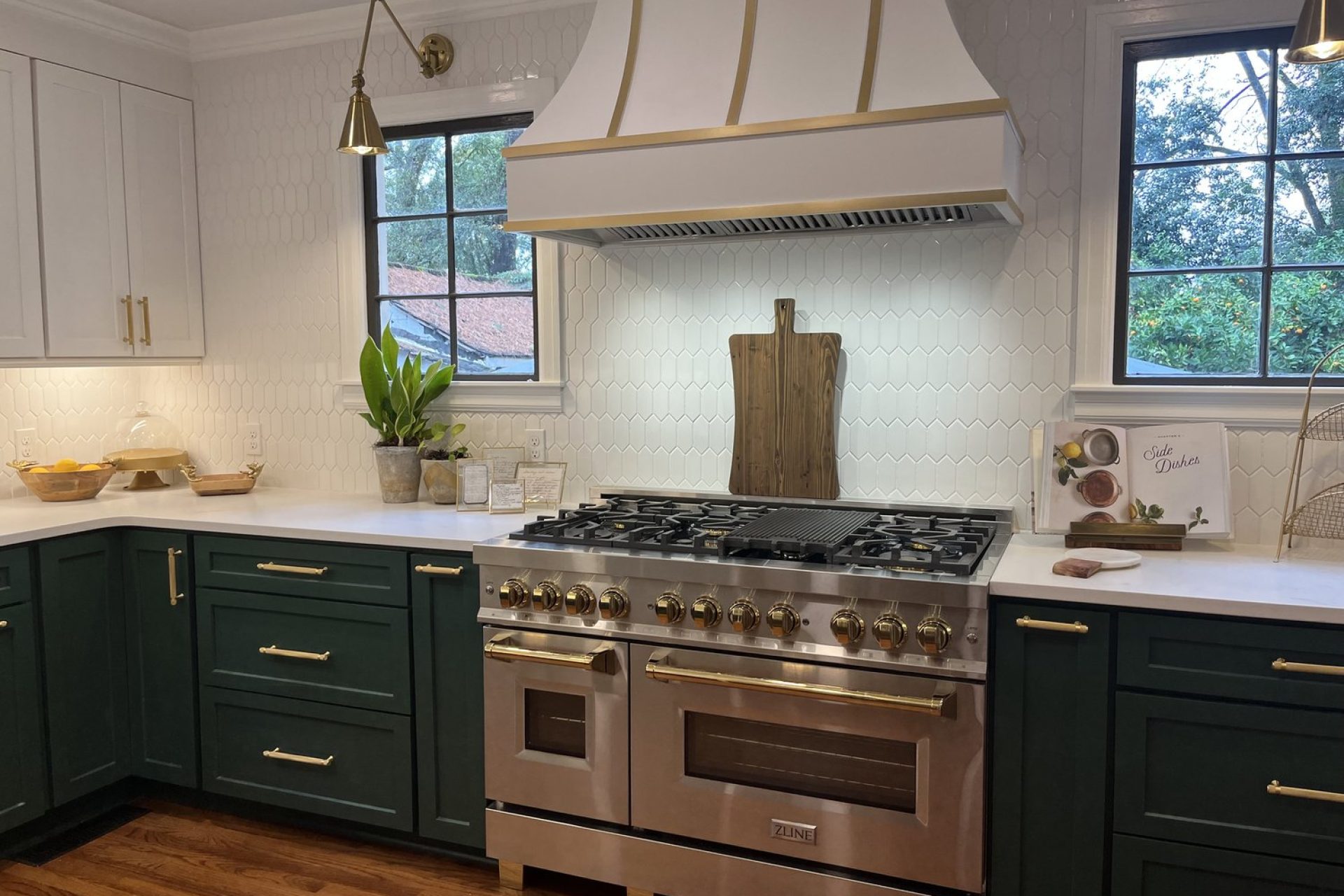 Luxury kitchen remodel featuring green lower cabinets, large stainless steel gas range, custom range hood, white tile backsplash, and gold accents, completed by Dorsey Builders in Dothan, Alabama.