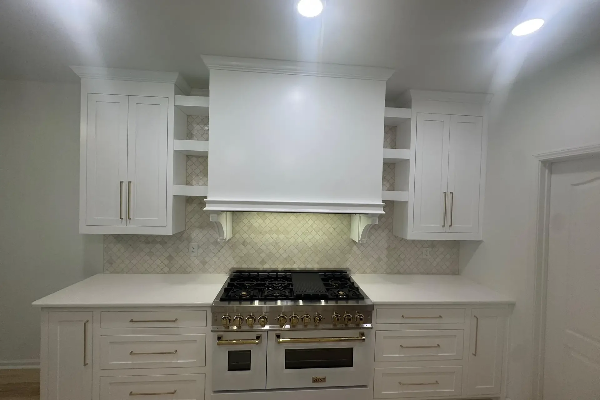 Custom kitchen with white cabinetry, built-in range hood, gold hardware, and detailed backsplash in Dothan, Alabama.