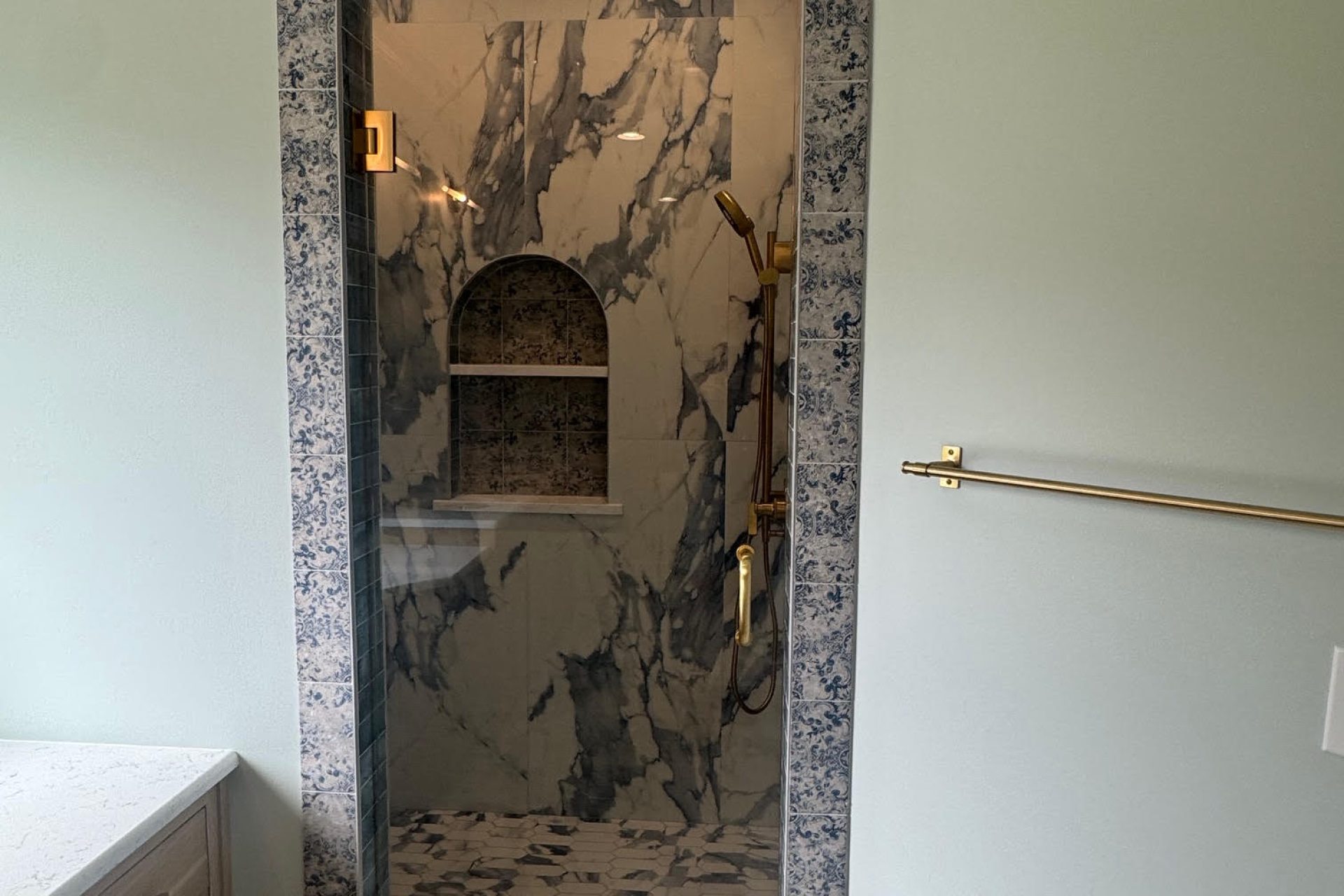 Custom marble walk-in shower with arched glass door and decorative tile border by Dorsey Builders in Dothan, Alabama.