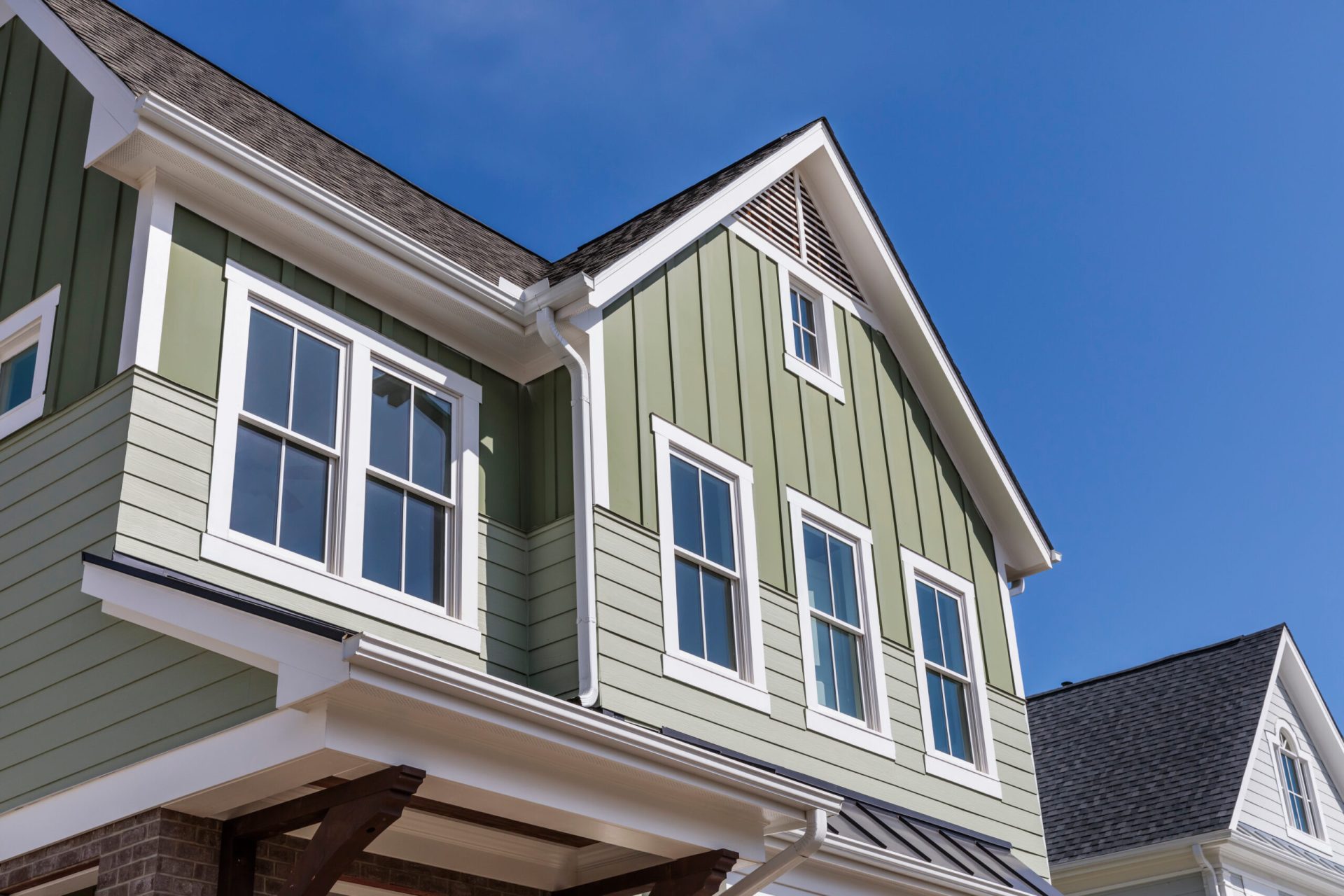 Custom-built green siding home with white trim and multiple windows under blue sky, built by Dorsey Builders in Dothan, Alabama.